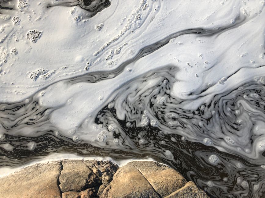 Close-up abstract view of swirling water surface with bubbles and rock texture.