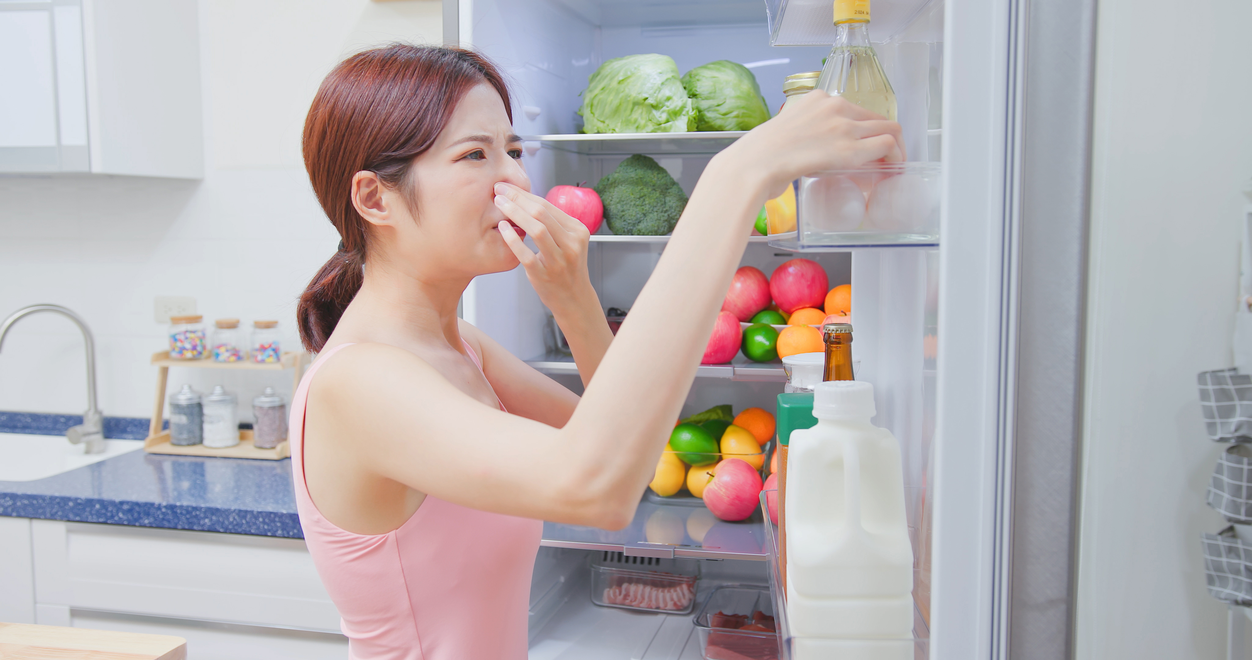 냉장고에서 나는 냄새에 코를 막고 있는 여성, 냉장고 내부에 채소와 과일이 가득한 모습