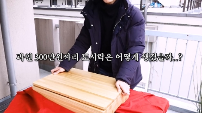 빨간 테이블 위에 있는 대형 나무 도시락을 여는 사람