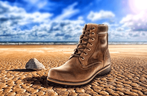 쩍쩍 갈라진 메마른 땅 위에 낡은 갈색 단화 한 개가 있다. 단화 옆에는 작은 회색 돌이 있다.