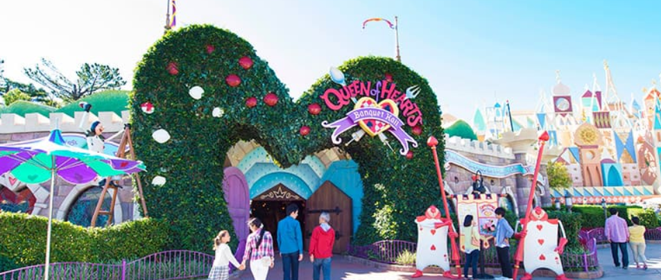 형형색색의 건물과 나무들이 있는 놀이동산 앞에 사람들이 서 있다.