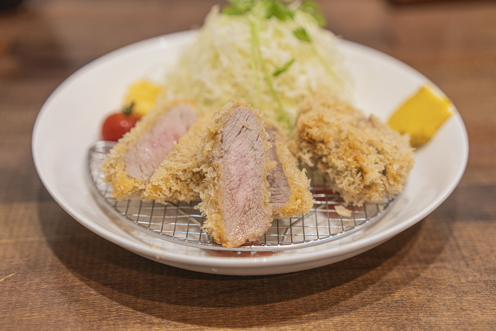 Jukusei Buta Kawamura: thick tonkatsu on a rack over a white plate, with the sliced cross section and shredded cabbage visible.