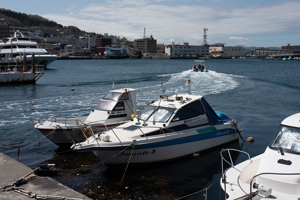일본 삿포로의 바다. 선박장에는 요트가 묶여있고 그 중 한 요트가 빠져나와 사람들을 태우고 저 멀리 파도를 만들며 나아가고 있다
