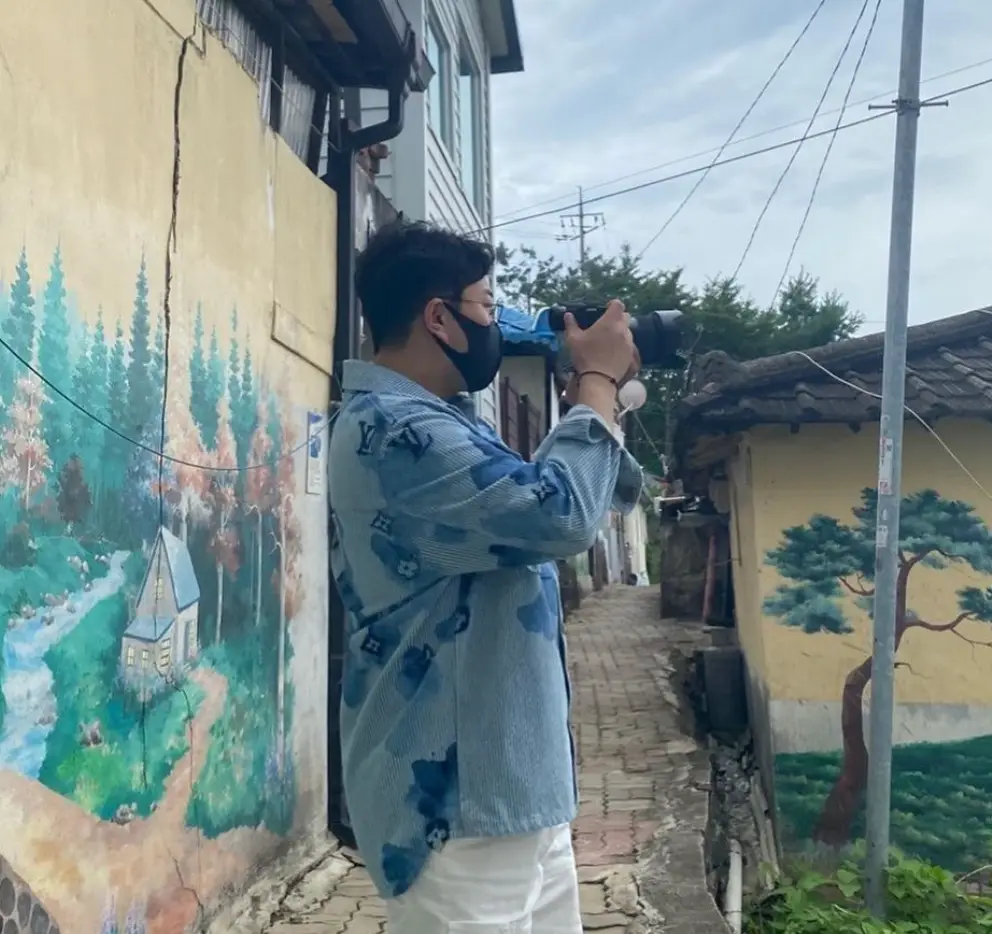 알록달록 벽화가 그려진 좁은 골목 파란 셔츠를 입고 카메라를 들고 사진찍는 김호중