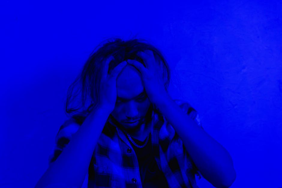 Portrait of a distressed person under dramatic blue lighting, expressing mental anguish.