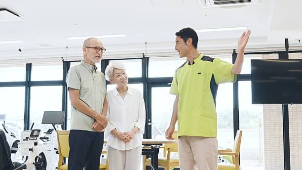 요양원 사무실로 보이는 곳에서 방문 차 온 듯한 시니어 남녀 두분이 직원의 설명을 듣고 있는 장면의 이미지
