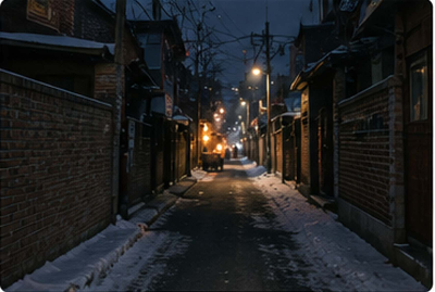 눈이 남은 어두운 겨울 골목 끝에 따뜻한 불빛을 내는 군고구마 노점이 보이는 모습