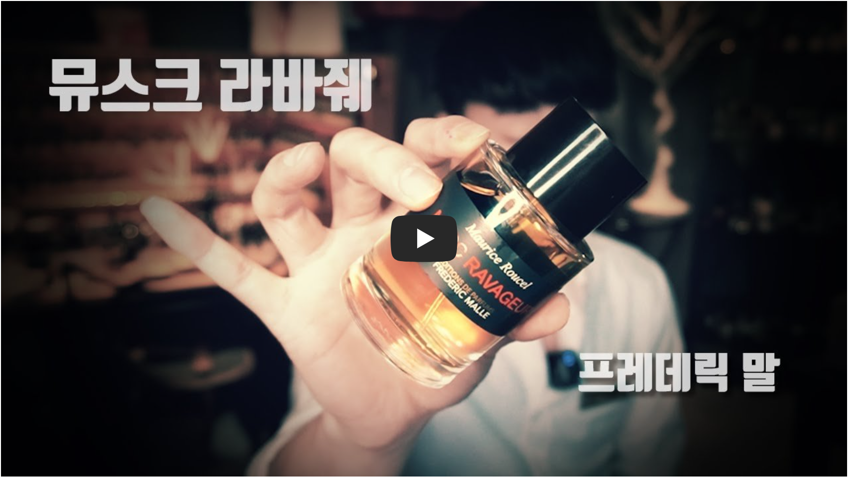 흐릿한 배경 속에서 한 사람이 손에 프레데릭 말(Frederic Malle)의 뮤스크 라바줴(Musc Ravageur) 향수병을 들고 카메라 쪽으로 보여주고 있다. 향수병에는 호박색 액체가 담겨 있으며, 화면 좌측 상단에는 ‘뮤스크 라바줴’, 우측 하단에는 ‘프레데릭 말’이라는 한글 텍스트가 굵게 표시되어 있다