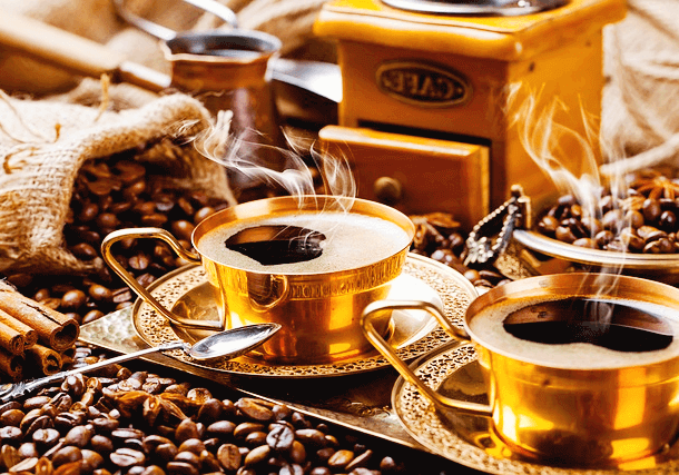 황금 찻잔 2개에 뜨거운 아메리카노 커피가 가득하다. 하얀 연기가 솔솔 난다. 주변엔 고동색 커피콩들이 가득하다.