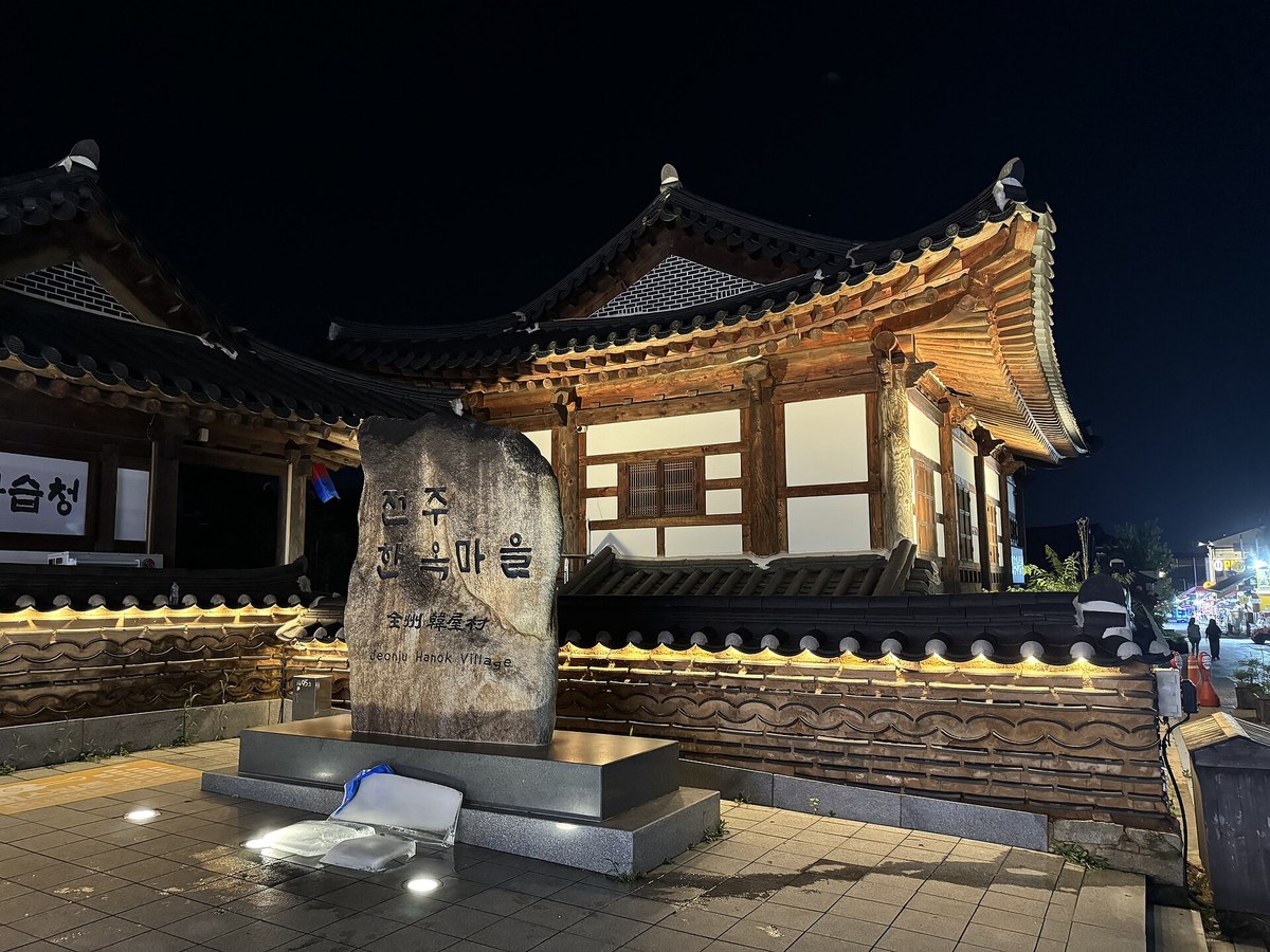 The Jeonju Hanok Village stone marker and a lit hanok building at night