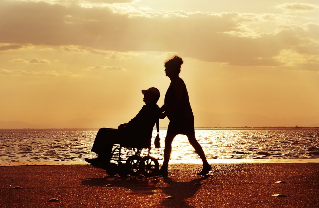 해변가에서 휠체어를 탄 남자와 휠체어를 밀어주는 여자 사진