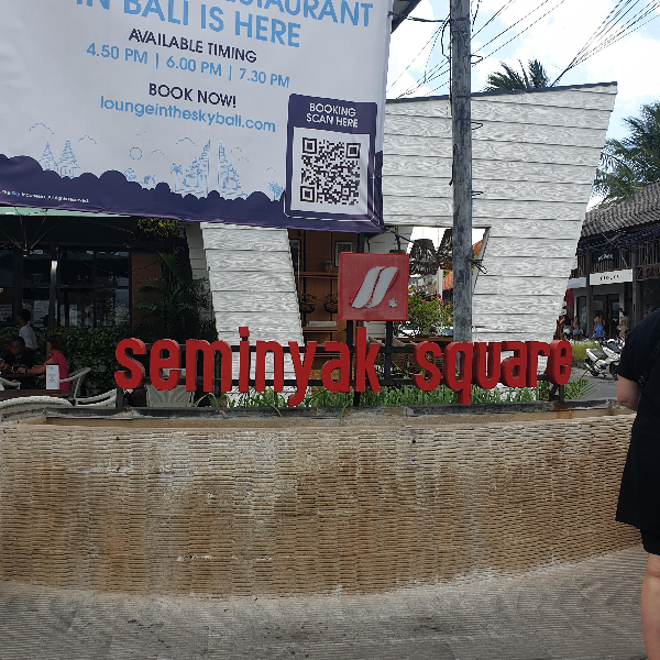건물 앞에 빨간색 Seminyak Square 간판이 보인다. 큰 광고 현수막이 내려와있다.