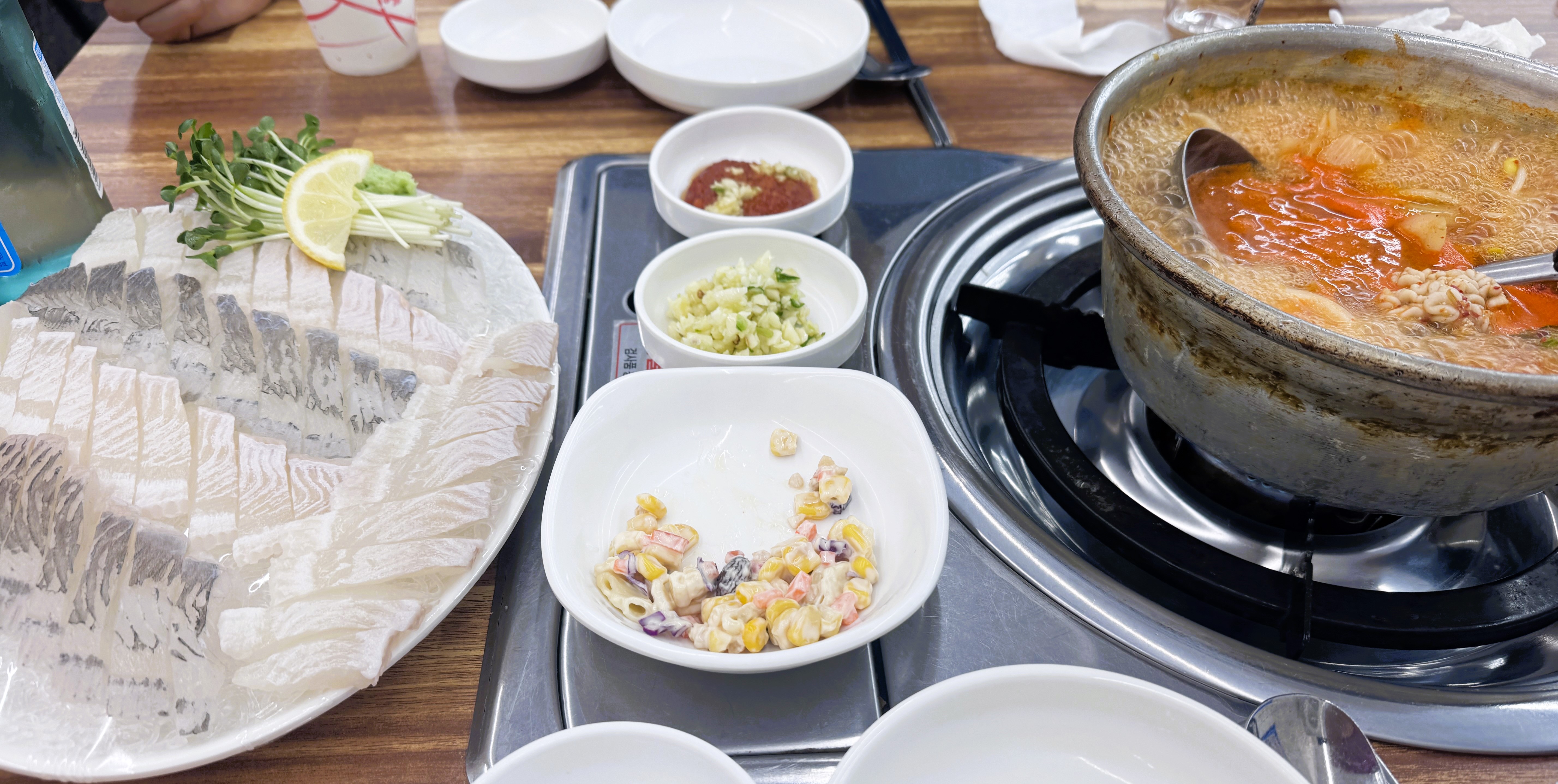 도다리회 한 접시와 끓고 있는 알탕, 기본 반찬들이 함께 차려진 테이블 상차림 모습 회와 빨간 국물의 탕 조합 사진