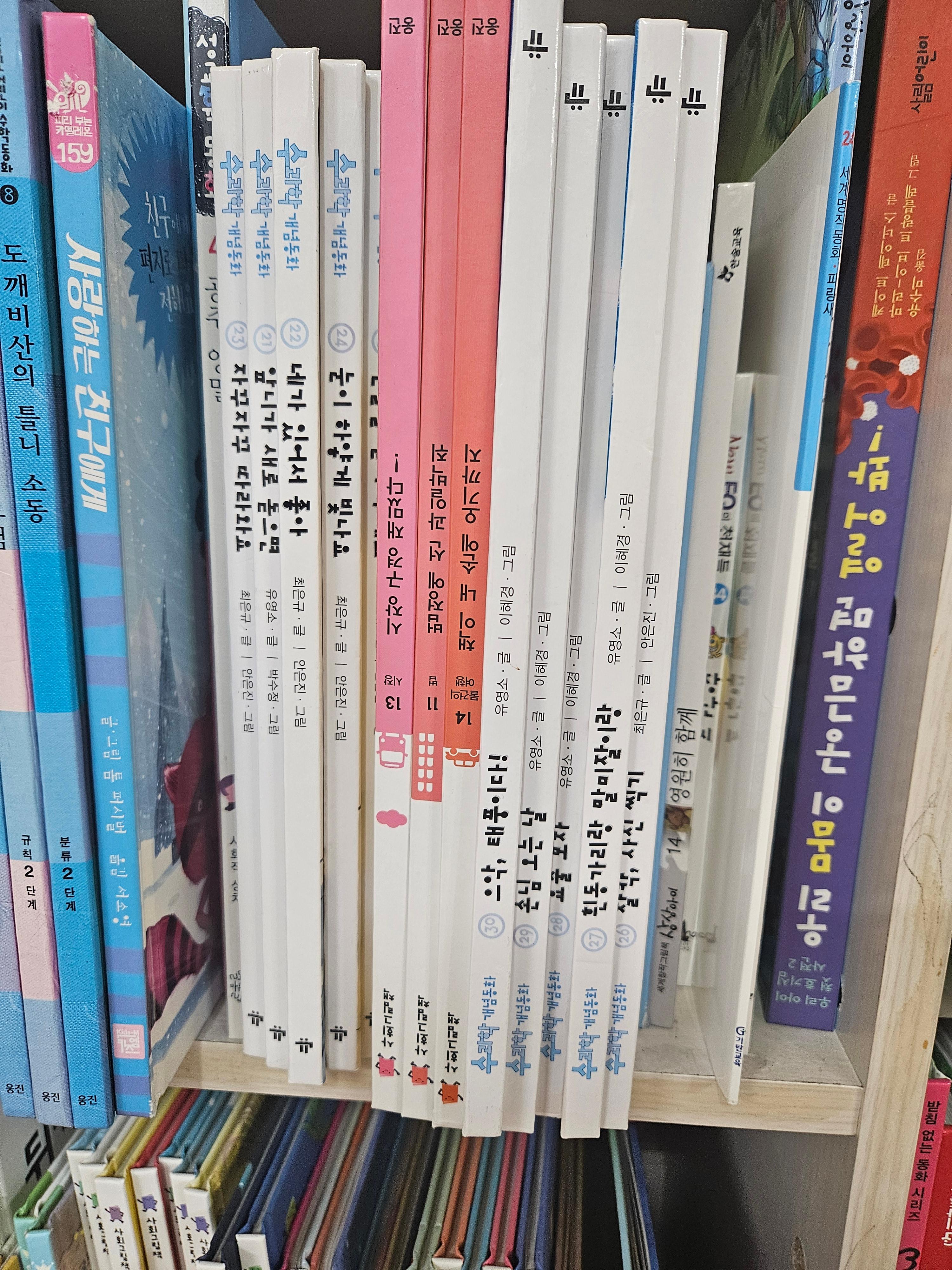 초등학생 책장에 파란색, 분홍색 전집들이 똑바로 꽂힌 모습과 거꾸로 뒤집혀 꽂힌 책들이 섞여 있는 모습