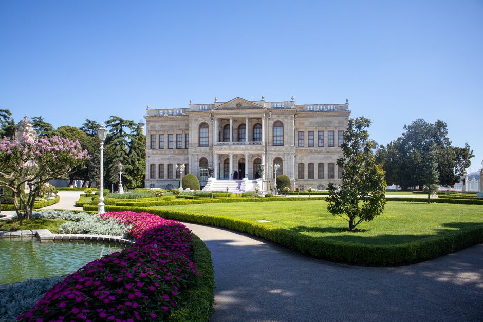 Dolmabah&ccedil;e Palace with manicured gardens under a bright blue sky in Istanbul, Turkey.