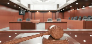 나무 판결봉이 테이블 위에 놓여 있고, 법정 내부가 보이는 이미지.