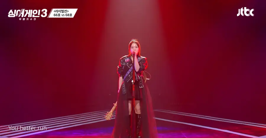 싱어게인3- 검은색 가죽자켓에 검은색 미니스커트 검은색 가죽부트를 신고 스탠딩마이크를 잡고 기타를 뒤로맨채 노래하는 66호