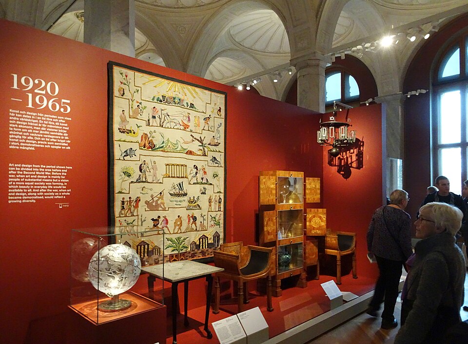 스톡홀름 Nationalmuseum의 1920~1965년 디자인 전시실, 붉은 벽을 배경으로 가구와 유리공예, 직물과 장식예술 작품이 함께 전시된 모습