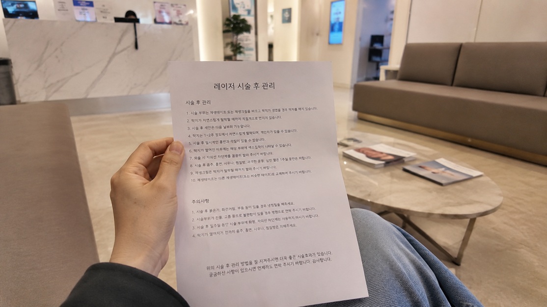 피부과 대기실 소파에서 레이저 시술 후 관리 및 주의사항 안내문을 들고 있는 모습