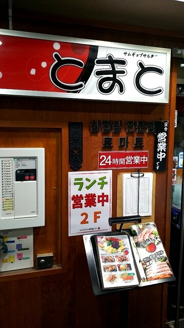 나무 벽에 일본어로 토마토라고 적혀 있는 간판이 걸려고 아래에 삼겹살 전문점 토마토라고 한국어로 적혀있다.