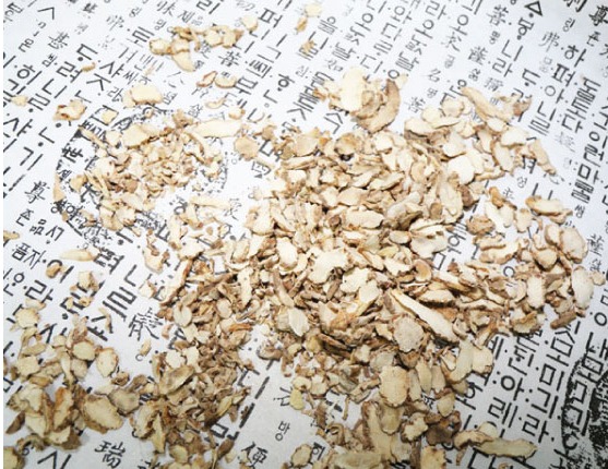 야생에서 채취를 한, 대왕풀의 뿌리인 백급을 잘 세척을 해서 건조한 후에 편으로 썰어서 옛 글자가 새겨진 종이 위에 펼쳐놓은 사진