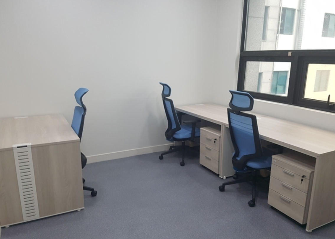 창문이 있는 3인 사무실 내부. 책상 3개 의자 3개가 놓여 있다