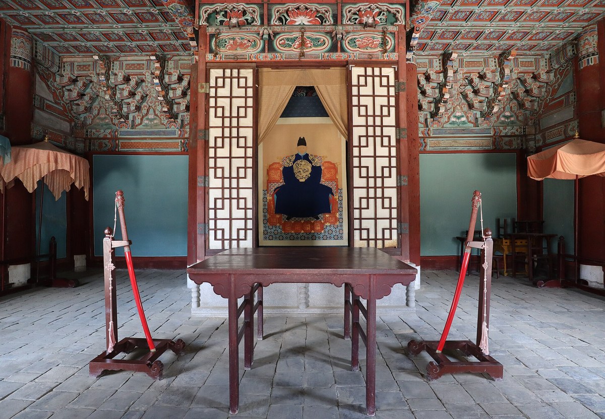 Inside a Gyeonggijeon hall, a portrait of King Taejo seen between lattice screens behind a red table