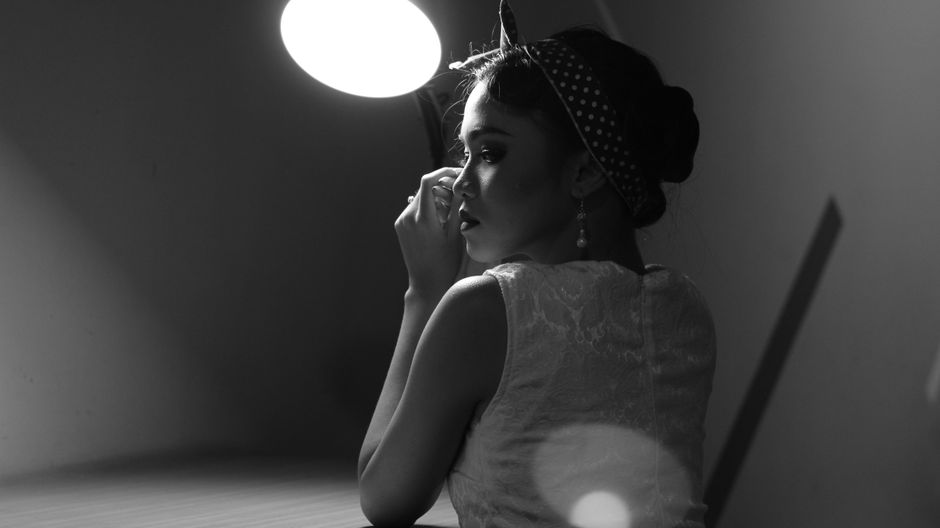 Elegant woman in a polka dot headband posing under a lamp, captured in black and white.