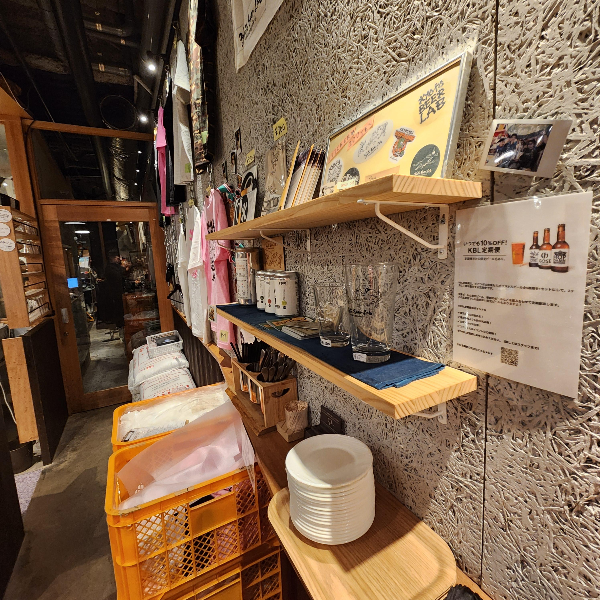 멀리 문이 보이고 그 입구는 좁다. 선반에 다양한 굿즈들이 놓여있다.