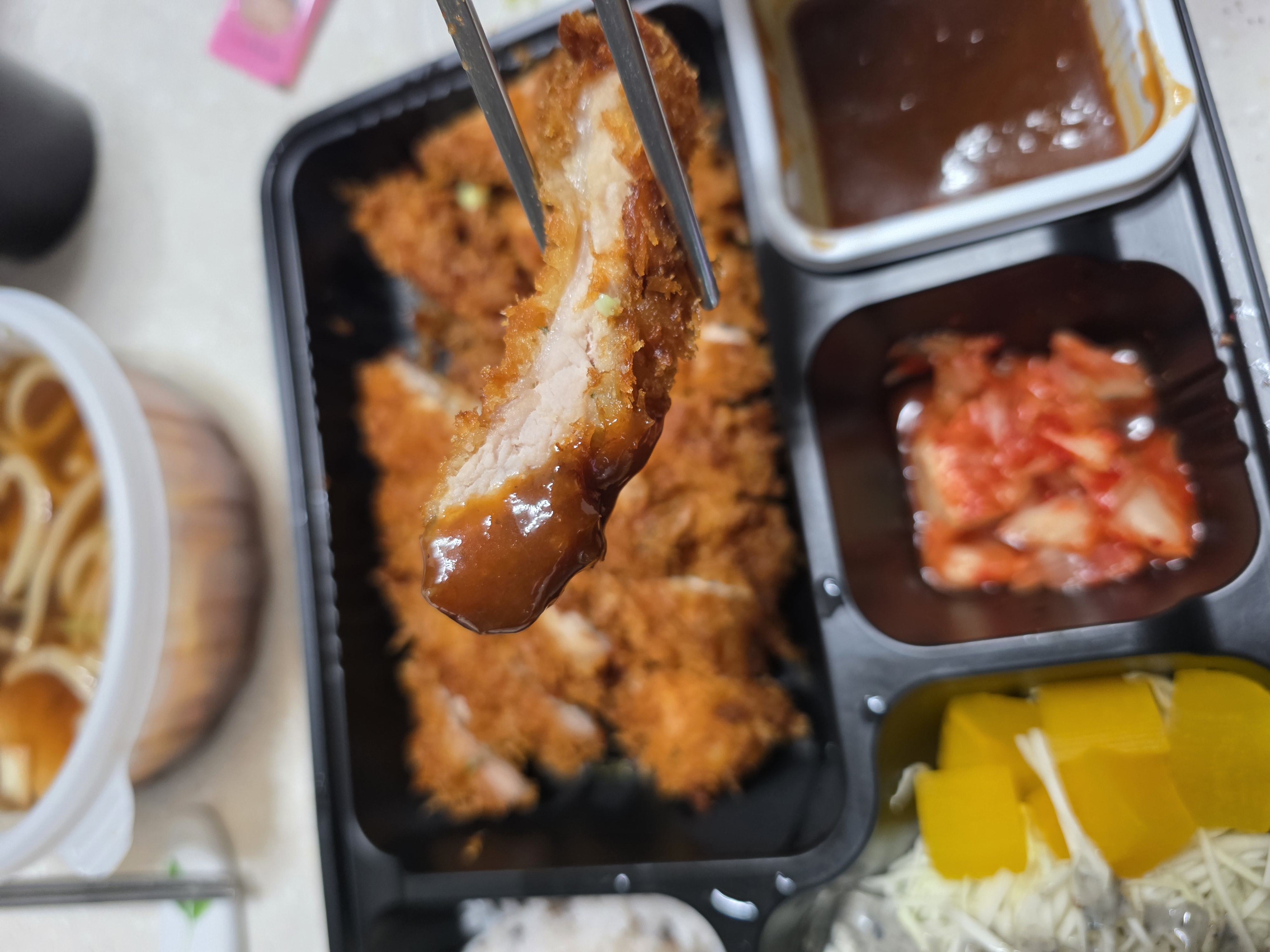 젓가락으로 들어 올린 돈까스 한 조각의 바삭한 튀김옷과 속살