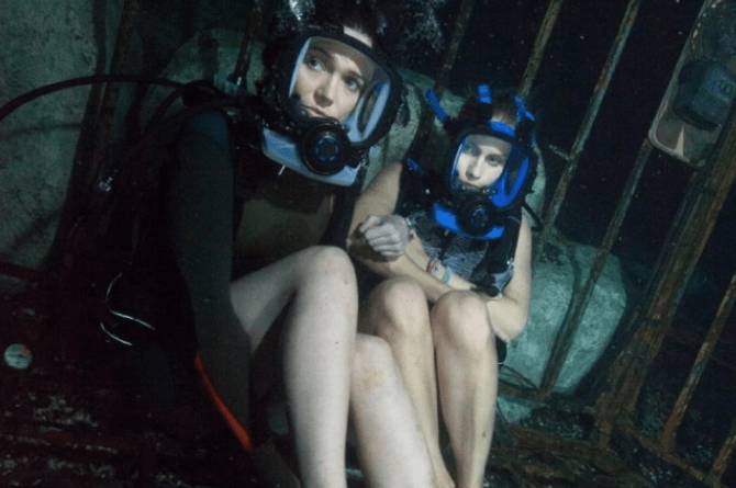 산소 마스크를 쓴 두 여성이 녹슨 철창 안에서 공포에 질린 채 앉아 있는 장면, 영화 〈47미터〉