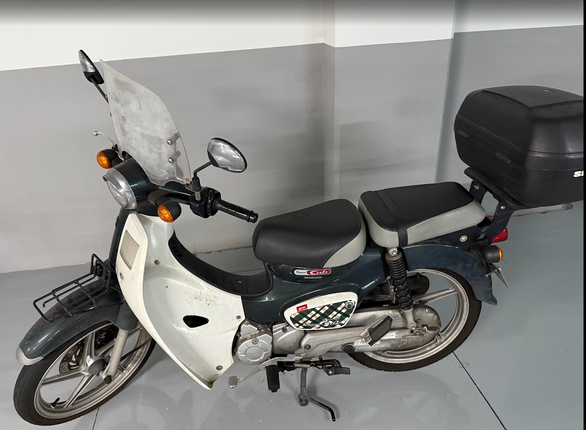 혼다 슈퍼커브 사진이고 전면부에 바람막이와 뒤에는 리어박스가 장착된 모습