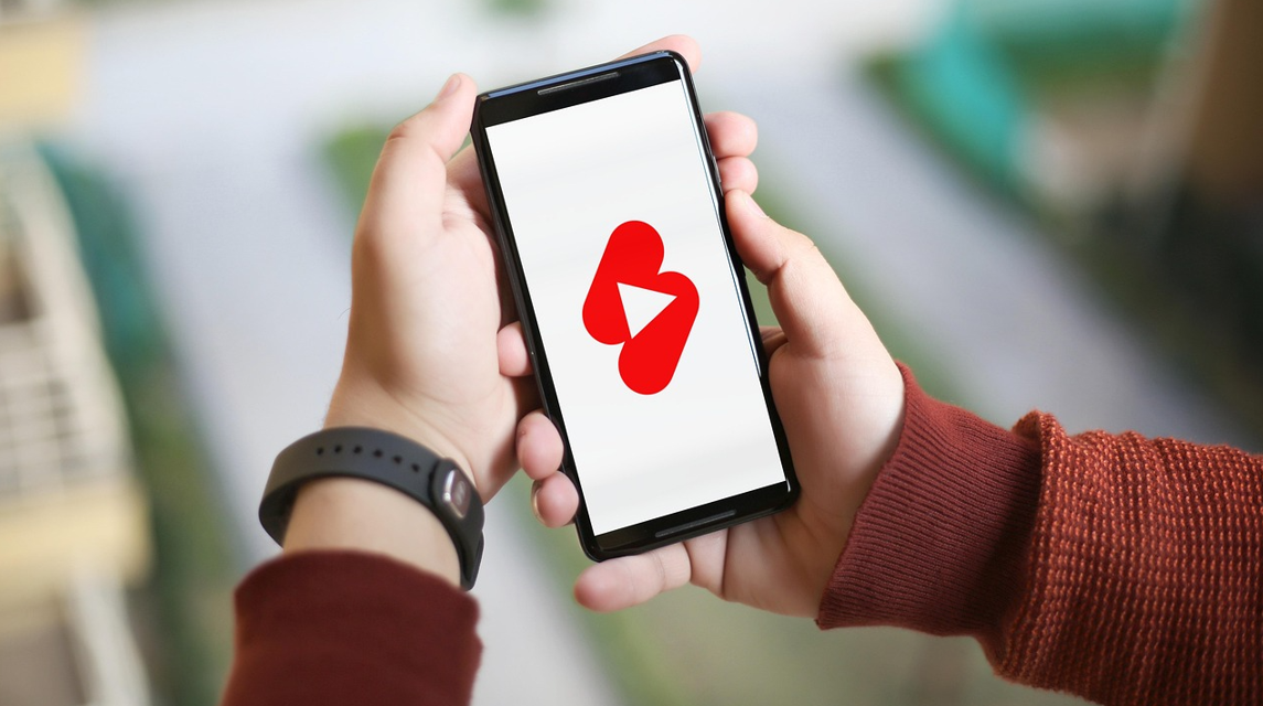 손에 휴대폰을 들고 있고 휴대폰 화면에 유튜브 쇼츠 가 보인다