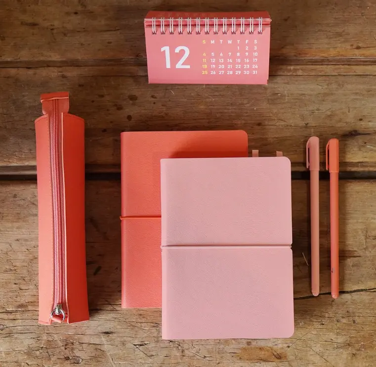 핑크색-리훈-다이어리가-책상-위에-놓여있고-그-옆에-필통과-연필이-보이는-사진