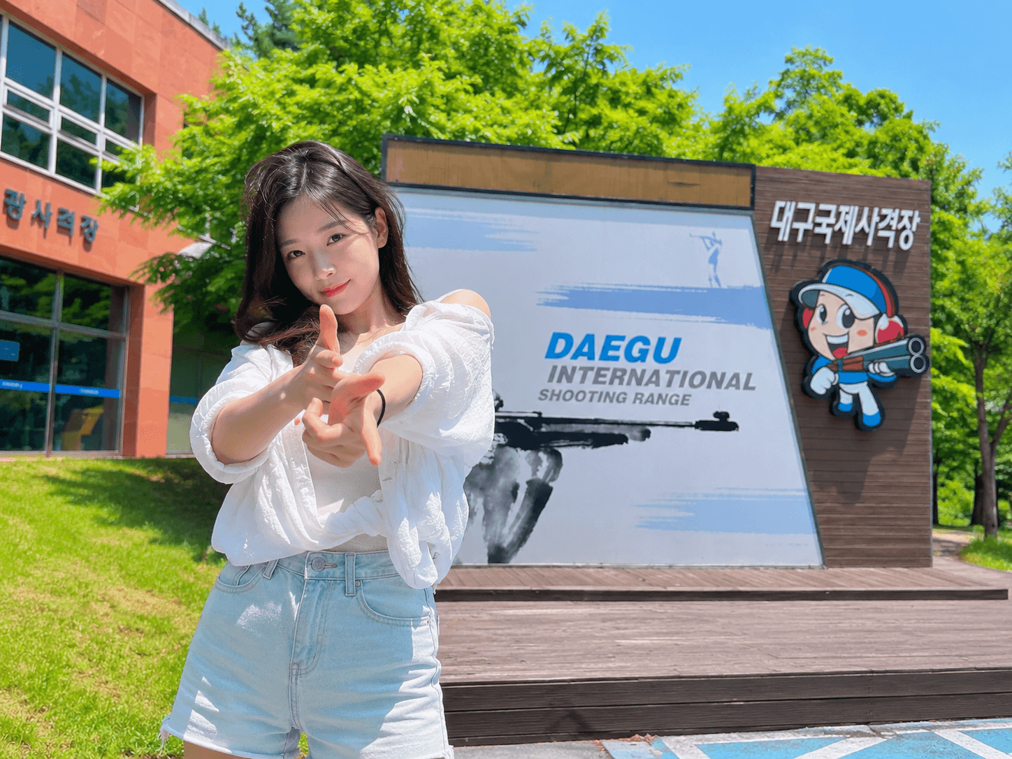 대구 북구 금호동 대구국제사격장 입구에 DAEGU INTERNATIONAL SHOOTING RANGE 안내판과 사격 캐릭터 조형물이 설치되어 있고 뒤편에 건물과 푸른 나무가 보이는 맑은 날 전경