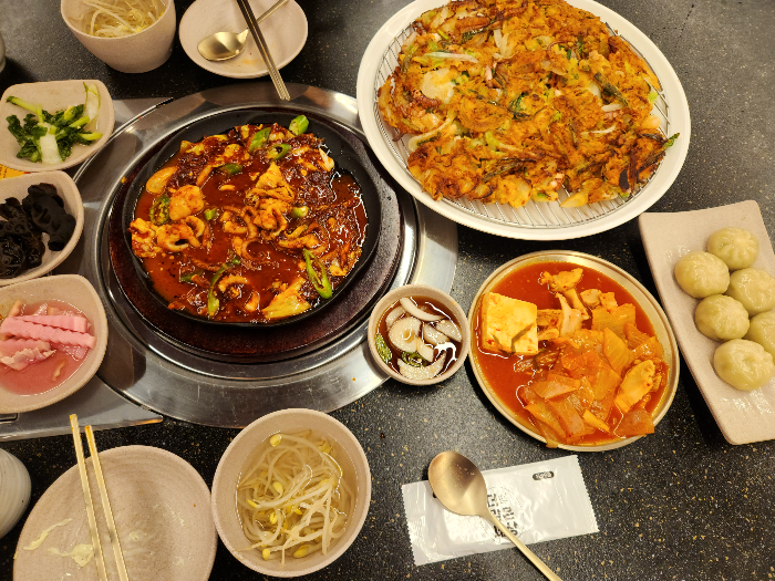 낚지볶음과 파전&#44; 만두&#44; 반찬들이 담긴 접시가 테이블 위에 있다