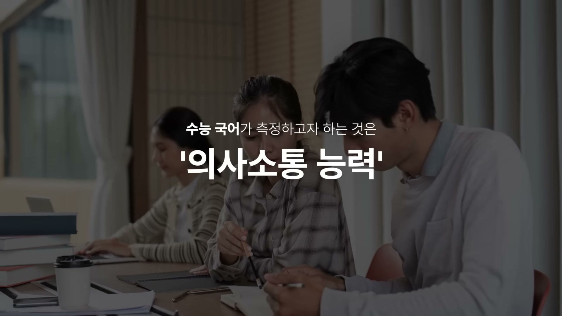 강의실에서 공부하는 학생들 위에 흰 글씨로 '수능 국어가 측정하고자 하는 것은 / 의사소통 능력' 텍스트가 표시된 슬라이드