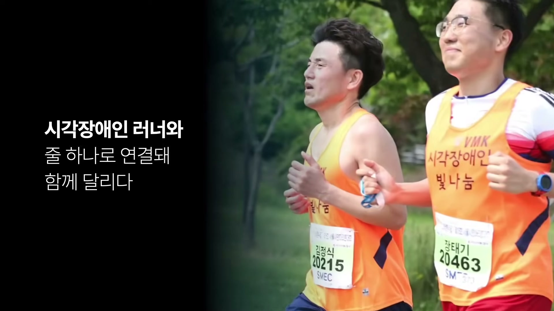 오렌지색 빛나눔 조끼를 입은 두 명의 러너가 손을 잡고 함께 달리는 모습