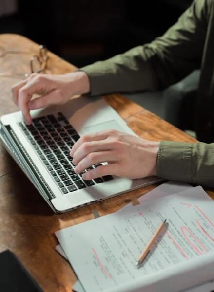 노트에 시놉시스를 정리하며 노트북으로 시나리오를 집필 중인 신인 영화 작가의 모습