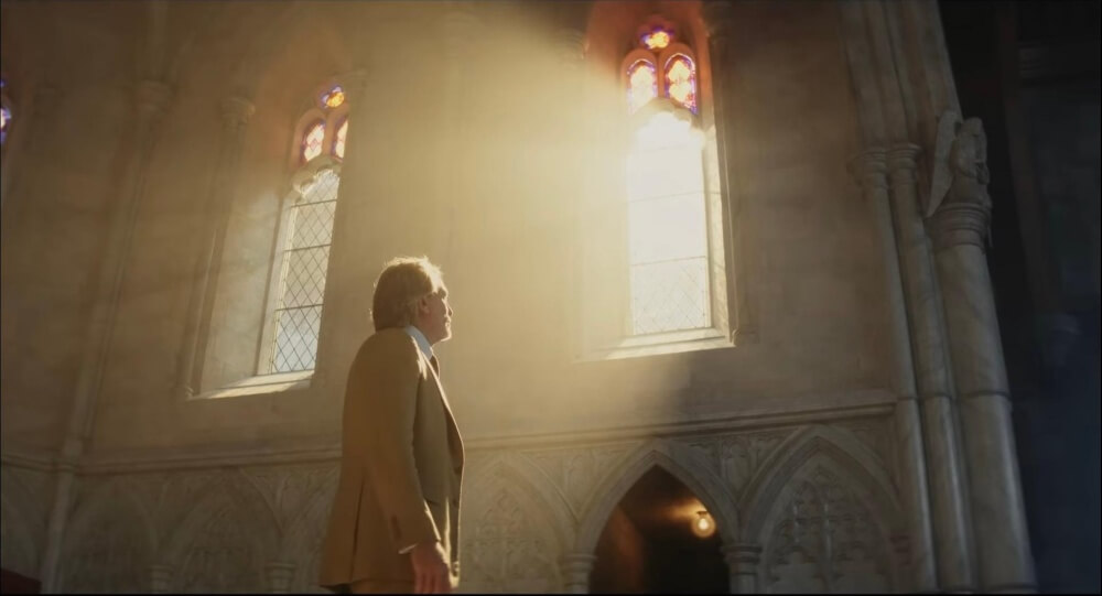 영화 나이브스 아웃3: 웨이크 업 데드 맨 스틸컷 – 탐정 브누아 블랑이 성당의 강렬한 창문 빛을 바라보는 장면