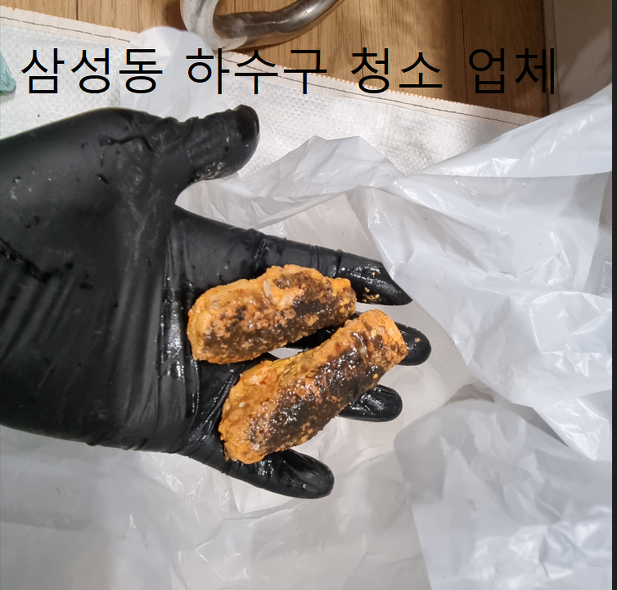 삼성동 하수구 청소 업체가 배관에서 꺼낸 기름 찌꺼기 덩어리를 장갑 위에 올려 놓은 모습