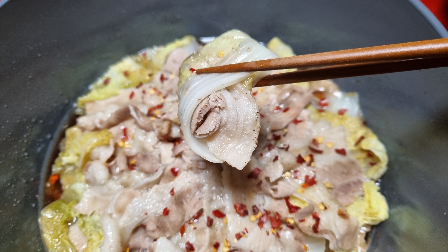 삼겹살 배추찜 한점을 젓가락으로 들고 있는 모습을 찍은 사진