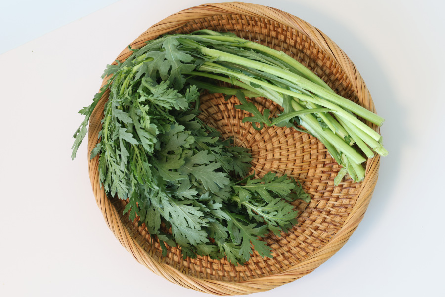 야생에서 채취를 한 쑥갓을 깨끗하게 세척한 것을 흰색 바닥 위에 대나무로 만든 동그란 바구니에 10여개 놓아두고 찍은 사진