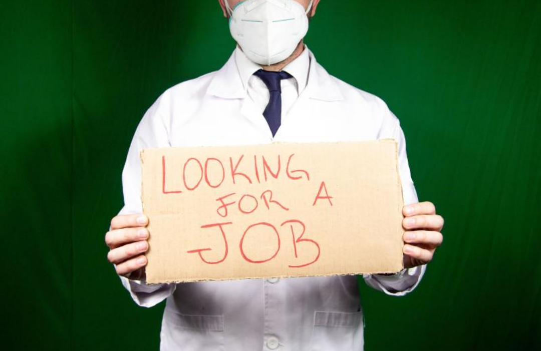 마스크를 쓴 한 남자가 직업을 구한다고 영어로 쓴 팻말을 들고 있다.