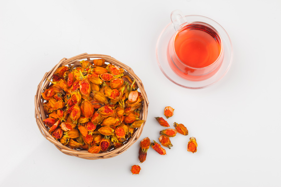 야생에서 채취를 한 치자를 깨끗하게 세척한 후에 바싹 말린 것을 흰색 바닥 위에 대나무로 만든 동그란 바구니에 가득 담아두고 그 옆에는 투명한 찻잔에 치자차를 반쯤 담아두고 그 밑에는 차자를 여러 개 바닥에 놓아두고 찍은 사진