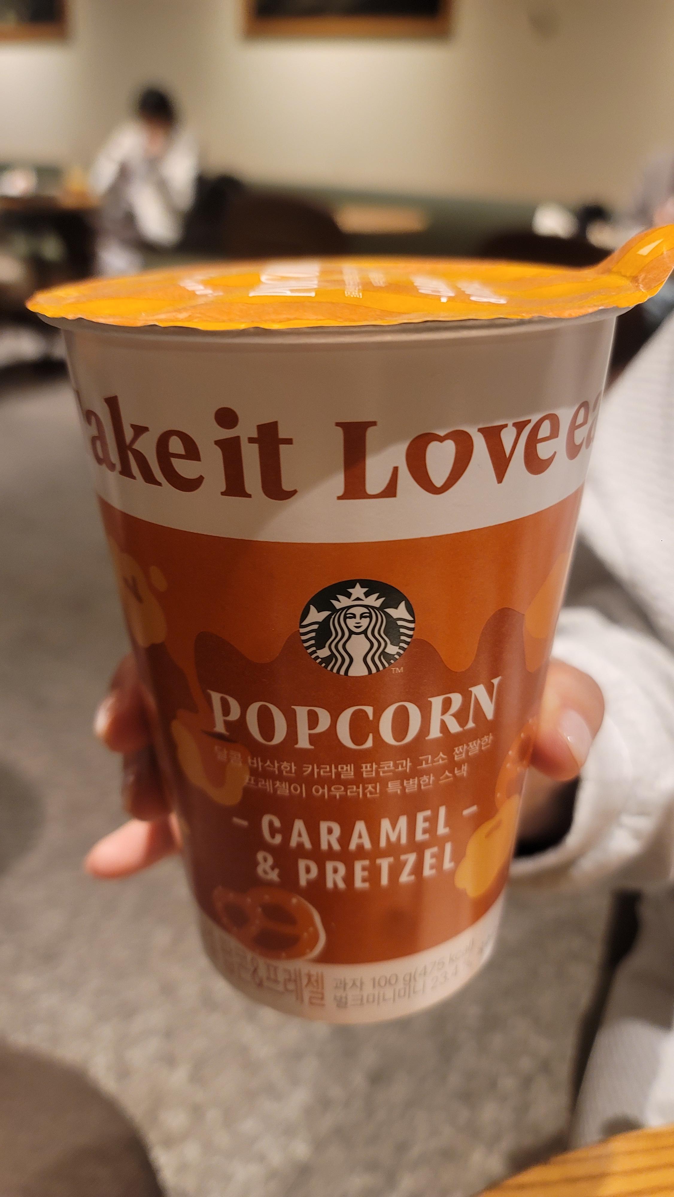 카페 테이블 위에서 손에 들려 있는 스타벅스 브랜드의 오렌지색·흰색 포장컵