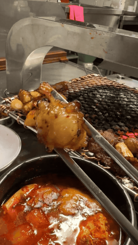 세광양대창 정자점 불판 위에서 노릇하게 구워진 대창을 젓가락으로 들어 올리는 장면&amp;#44; 바삭한 겉면과 윤기 흐르는 속살이 대비되어 식욕을 자극하는 모습