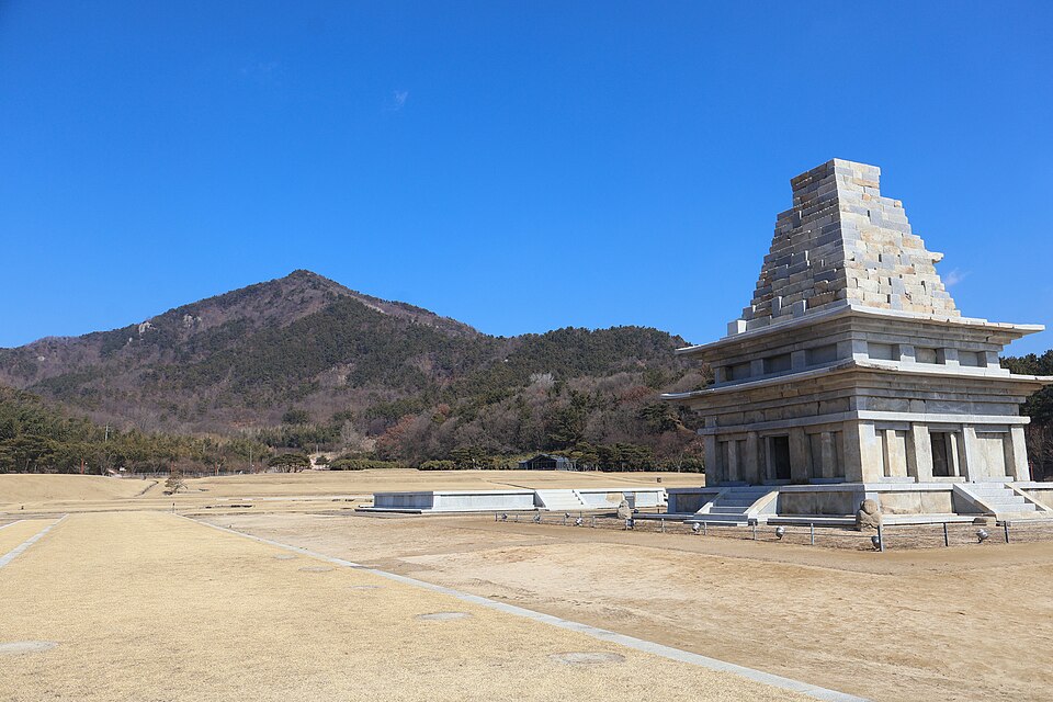 Mireuksa’s stone pagoda rises beside open temple-site foundations and dry grass, with wooded hills beneath a blue sky.