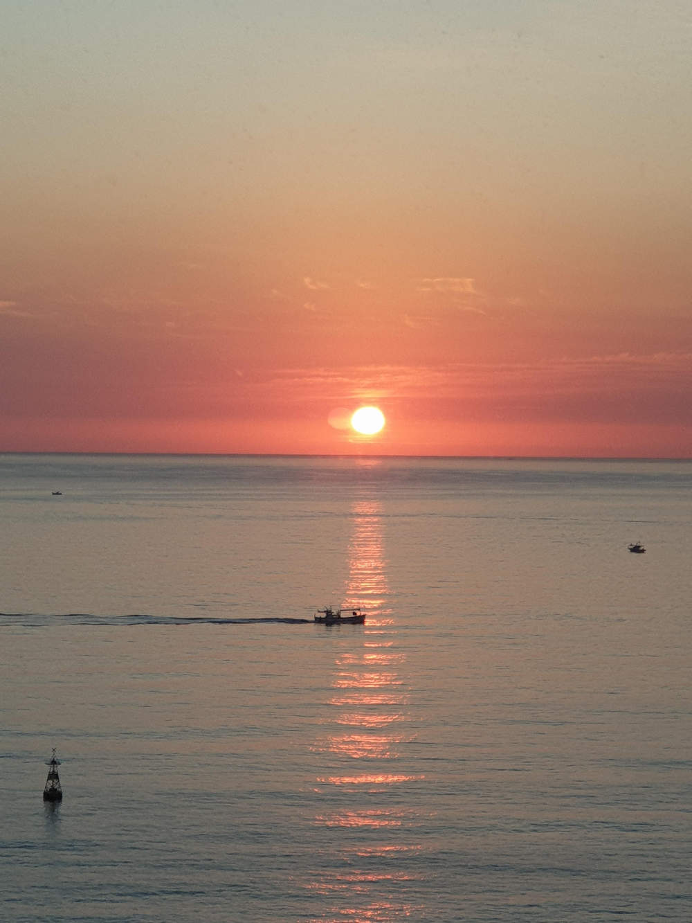 수평선 위로 붉은 해가 떠오른 모습. 바다에 작은 배들도 떠 다닌다.