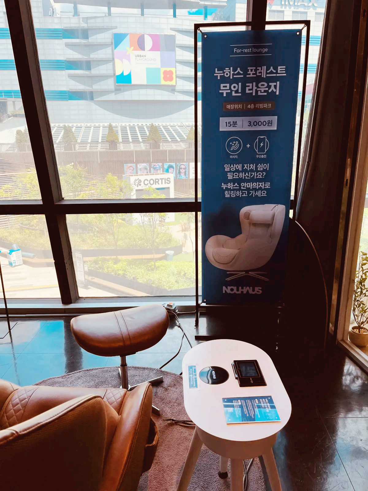 누하스 안마의자와 유리창으로 보이는 맞은 편 경치 그리고 누하스 포레스트 무인 라운지 배너